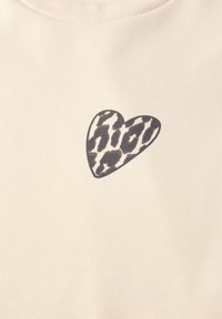 Tissu beige avec un petit motif de cœur en imprimé léopard centré près du haut.