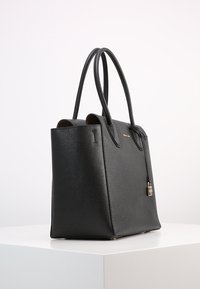 Sac fourre-tout en cuir noir avec un design structuré, double poignées, texture lisse et accent en cadenas doré. Base plate pour la stabilité.