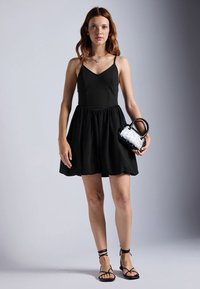 Vestido negro sin mangas con un torso ajustado y falda acampanada. Combinado con un bolso a rayas en blanco y negro y sandalias negras con tiras.