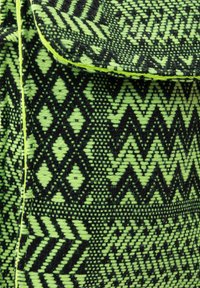 Bolso de tela estampada con un vibrante diseño geométrico en verde y negro, con diamantes y chevron, cosido con un borde contrastante.