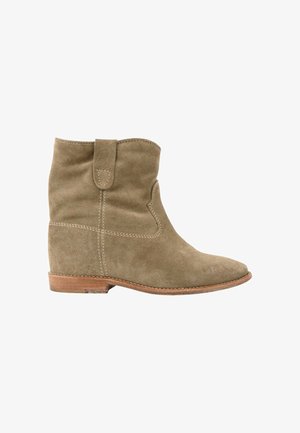 Bottine en daim beige avec un petit talon en bois et une languette, coutures visibles sur les côtés et à l'avant.
