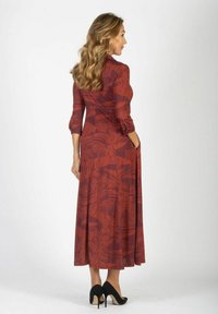 Czerwona maksi sukienka z krótkimi rękawami, ozdobiona wzorem roślinnym. Wykonana z gładkiego materiału, posiada kieszenie, uzupełniona czarnymi szpilkami.