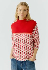 Rot und cremefarben gemusterter Strickpullover mit hohem Kragen, der ein Wellenmuster im unteren Bereich und lange Ärmel aufweist. Lässige Passform.