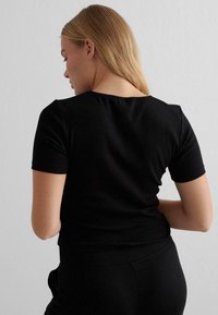 Schwarzes, kurzärmeliges, eng anliegendes T-Shirt mit rundem Ausschnitt. Der Stoff wirkt glatt und dehnbar und zeigt ein schlichtes Design mit klaren Linien.