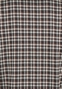 Tessuto a quadri marrone e bianco con un motivo a griglia e quadrati alternati. La texture appare tessuta, conferendo un aspetto robusto.