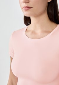 Jasnoróżowa bluzka z krótkim rękawem i okrągłym dekoltem, wykonana z gładkiego, elastycznego materiału; przylegający fason bez widocznych wzorów czy elementów metalowych.