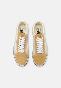 Zapatillas de ante marrón y lona crema con cordones blancos, presentan un diseño bajo y suelas de goma negras. Se aprecian múltiples detalles de costura.