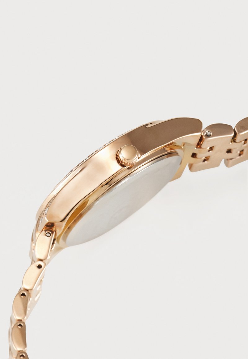 Montre bracelet en ton or avec un boîtier rond et une lunette texturée, dotée d'un cadran lisse de couleur claire et d'un bracelet en maillons en métal.