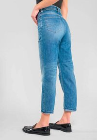 Jeans en denim bleu clair taille haute, coupe droite, avec deux poches arrière et des détails décolorés au niveau des cuisses. Texture lisse, longueur cheville.