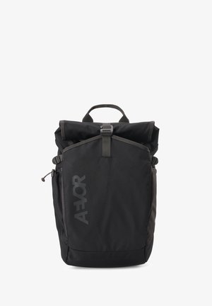Sac à dos noir à rabat enroulable avec boucle frontale, poche en mesh latérale et logo vertical AEVOR sur le panneau avant.