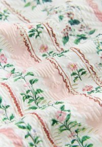 Tessuto trapuntato con strisce rosa e bianche, motivi floreali verdi a foglia e cuciture testurizzate che creano una superficie morbida e ondulata.