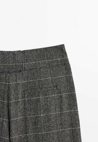 Pantalons en tartan gris avec un tissu texturé. Comprend une taille et un détail de poche latérale. Des lignes blanches contrastantes forment le motif à carreaux.