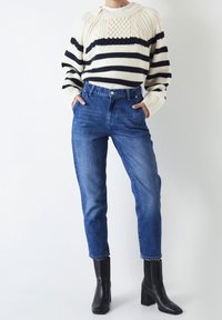 Maglione a righe lavorato a maglia in crema e blu navy, con pannelli testurizzati; jeans blu a vita alta; stivali neri alla caviglia con punta quadrata.