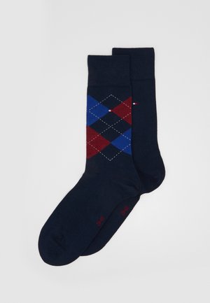 Navy socks featuring an argyle pattern in red and blue, made of soft fabric with a ribbed cuff and small logo detail in red.