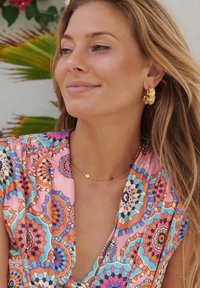 Robe colorée à motifs avec des designs géométriques en rose, bleu et orange. Boucles d'oreilles en or et un délicat collier en or. Texture douce.