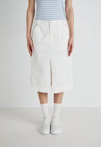 Hvit denim midi-skjørt med frontsplitt, beltestropper og sidelommer, kombinert med en blåstripet topp og hvite sneakers med sokker.