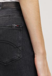 Svarta denimjeans har en bakficka med böjd sömnad, en liten märkespatch och ett etikett med röda, vita och blå detaljer.