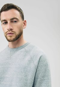 Grå crewneck sweatshirt med blød tekstur, der har en ribbet halsudskæring og raglanærmer. Simpelt design uden mønstre eller accenter.