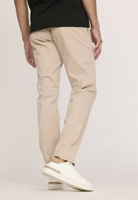 Pantalons beiges décontractés en tissu léger, avec une coupe décontractée. Associés à des baskets blanches avec une subtile touche de doré.