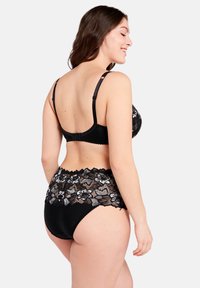 Bralette de encaje negro y bragas de talle alto a juego con patrones florales, con correas ajustables y bordes con forma de ondas.