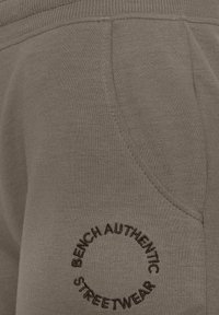 Primo piano di jogger grigi in cotone con tasca laterale e un logo circolare con "BENCH AUTHENTIC STREETWEAR" ricamato in contrasto.