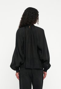 Black blouse with puffed sleeves, pleated back detail, and a keyhole opening at the neck. Made from lightweight, sheer fabric.