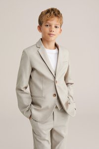 Šviesiai beige kostiumas su prigludusia švarku ir suderintomis kelnėmis. Yra išpjautas apykaklė, vieno mygtuko uždarymas ir subtili tekstūra.