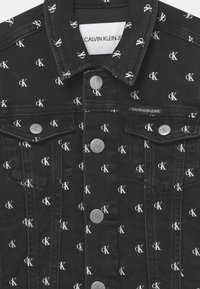 Giacca di jeans nera con un motivo a logo CK bianco su tutta la superficie, bottoni argentati e un design classico del colletto. Etichetta del marchio chiara all'interno.