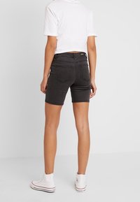 Shorts de mezclilla negros con un ajuste de cintura media, que presentan bolsillos traseros y un dobladillo justo por encima de la rodilla, combinados con zapatillas blancas de caña alta.