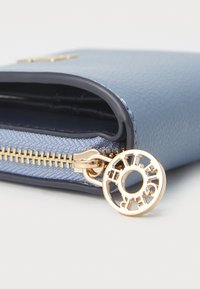 Blue textured leather wallet with gold zipper and circular charm. Features a smooth finish and contrasting navy accents.