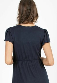Granatowa sukienka z krótkimi bufiastymi rękawkami, miękka tkanina, marszczona talia i okrągły dekolt, ukazująca widok z tyłu oraz minimalne detale projektu.