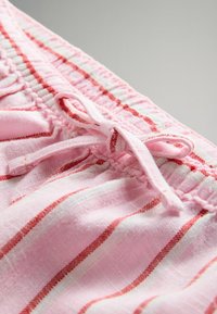 Pantaloni corti di cotone rosa con righe orizzontali rosse, dotati di vita elastica arricciata e dettaglio a fiocco sul davanti. Tessuto testurizzato.