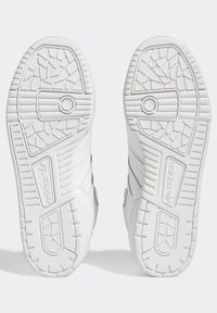 Weiße Adidas-Sneaker von der Sohlenseite gezeigt, mit strukturierten Grip-Mustern und Adidas-Logo auf jeder Sohle.