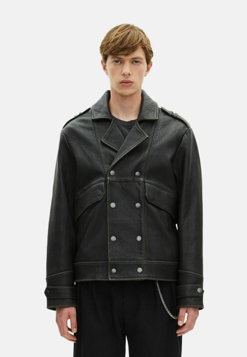 Chaqueta de cuero negra con diseño de doble botonadura, botones plateados y costuras verdes. Cuenta con grandes bolsillos y un detalle de cadena en el dobladillo.