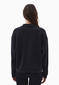 Sudadera negra de corte relajado, con costuras de hombro bajas, puños de canalé y un dobladillo ligeramente curvado. Textura de tela suave.