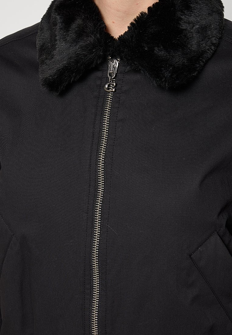 Czarna kurtka z miękkim kołnierzem z imitacji futra, z przodem na zamek błyskawiczny i bocznymi kieszeniami. Gładki materiał o matowym wykończeniu.