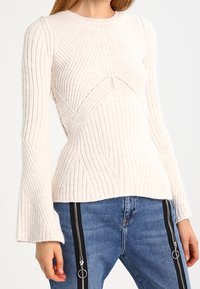 Lichtbeige geribde gebreide trui met een aansluitende silhouette, ronde hals en uitlopende mouwen. Bevat geometrische patronen en een gestructureerde stof.
