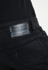 Svarta denimjeans med en texturerad yta. Har en blank rektangulär etikett på bakfickan med varumärke och skötselinformation.