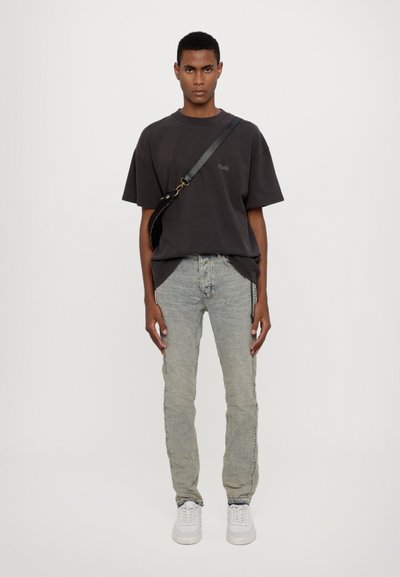 Overwymiarowy ciemnoszary t-shirt z bawełny z detalami bocznych szwów, w połączeniu z jasnoniebieskimi dżinsami o wyblakłej strukturze i zamkami. Białe trampki.