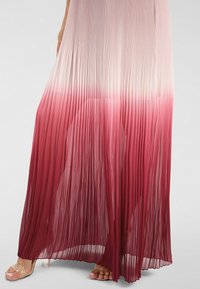 Plissiertes Maxikleid in einem Farbverlauf von hellrosa bis tiefburgunderrot, gefertigt aus einem leichten Stoff mit fließendem Design und transparenter Textur.