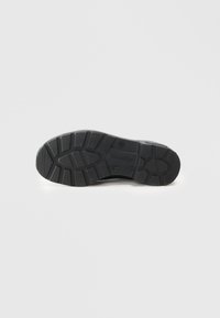 Semelle de chaussure en caoutchouc noir avec des motifs de texture, présentant des rainures profondes et des marques. Conception plate adaptée à diverses surfaces.
