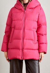 Chaqueta acolchada color fucsia brillante con capucha, que presenta una cremallera frontal completa, dos grandes bolsillos frontales y un patrón acolchado. Textura suave.