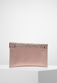 Käsilaukku pehmeää vaaleanpunaista nahkaa, jossa on kimaltava ruusukultainen yläosa. Suorakaiteen muotoinen, sileä pinta ja hillitty kiilto.