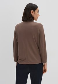 Haut marron à manches longues avec une texture lisse et un col rond, présentant une coupe décontractée et des détails de couture subtils à l'arrière.