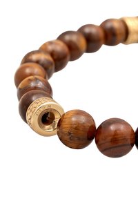 Pruun tiger's eye'iga helmes, mis sisaldab poleeritud sfäärilisi helmeid koos kuldse aksessuaarse klamberiga, millel on graveeritud mustriga disain.