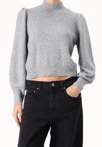 Grijze gebreide trui met hoge nek, gepofte lange mouwen en een cropped snit. Gecombineerd met zwarte high-waisted jeans met koperen accenten.