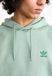 Lichtgroene hoodie van katoenmix, met een kangoeroezak en trekkoorden. Opvallende accenten zijn een geborduurd Adidas-logo.