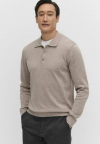 Beige pitkähihaisen polo-paidan, jossa on kaulus, kolme nappia ja ribbikuvioidut hihansuut. Paita on päällä valkoisen pyöreäkauluksisen t-paidan. Rentoa fiilistä pehmeällä rakenteella.