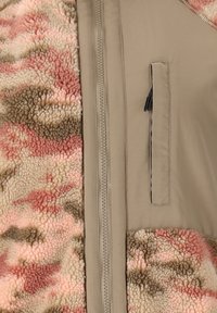 Närbild av en jacka med en beige dragkedja och ficka på en slät tyg bredvid ett mjukt, flerfärgat fleece-material i rosa, beige och brunt.