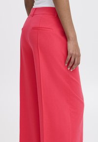 Pantalons à jambes larges en tissu rose vif, présentant une texture lisse, deux poches arrière et une taille haute.